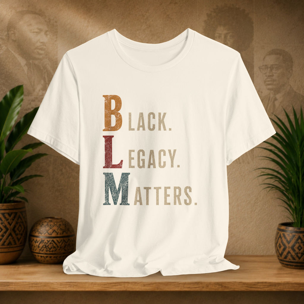 A beige short-sleeve T-shirt displayed on a wooden surface, featuring a distressed typographic design that reads 'BLACK LEGACY. MATTERS.