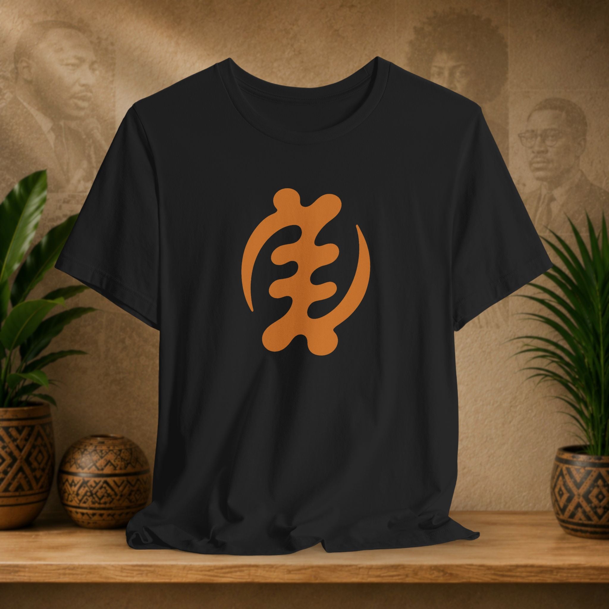 Black t-shirt with orange symbol on a wooden surface with plants and a textured wall background