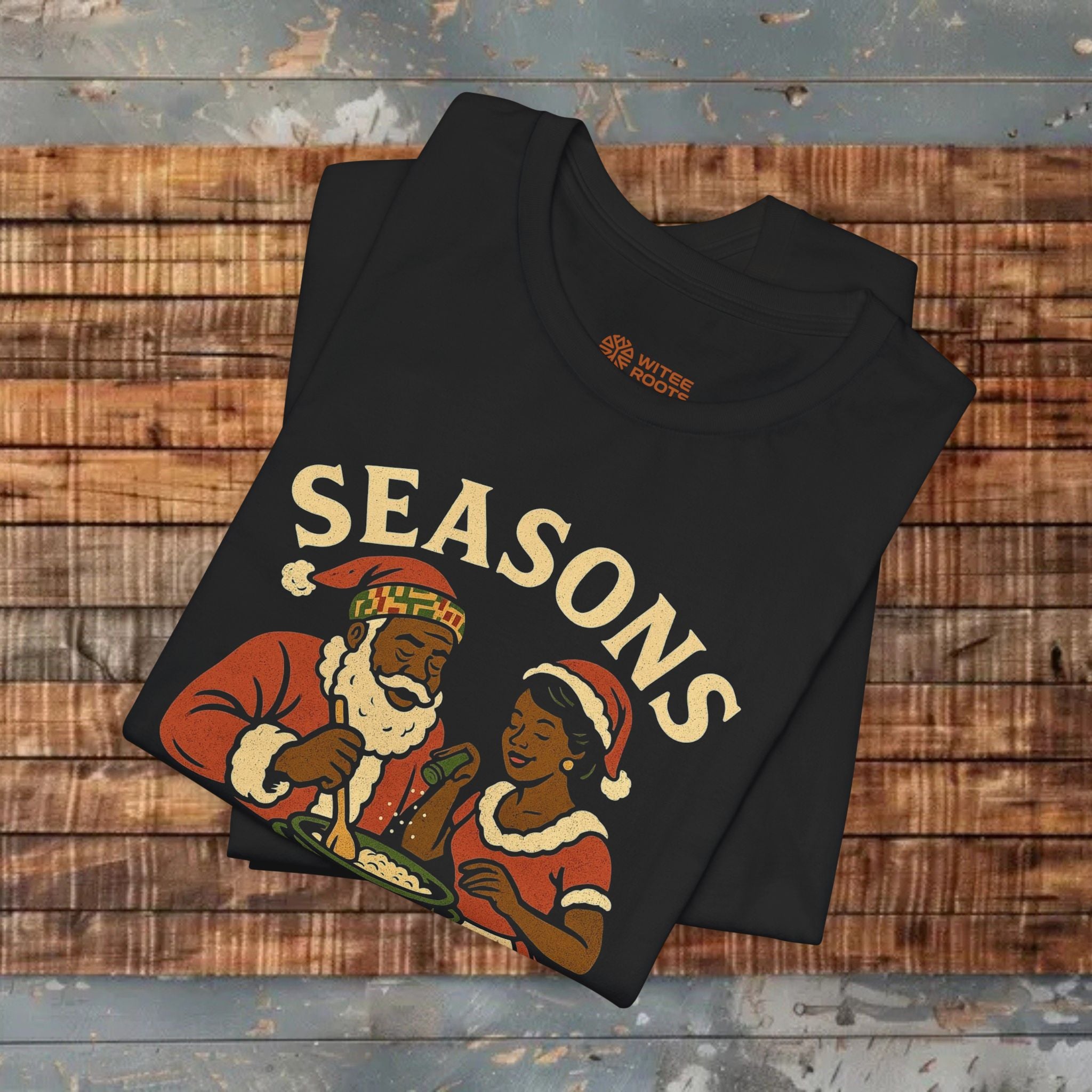 Black t-shirt with festive design featuring a man and woman in Santa hats on a wooden surface.