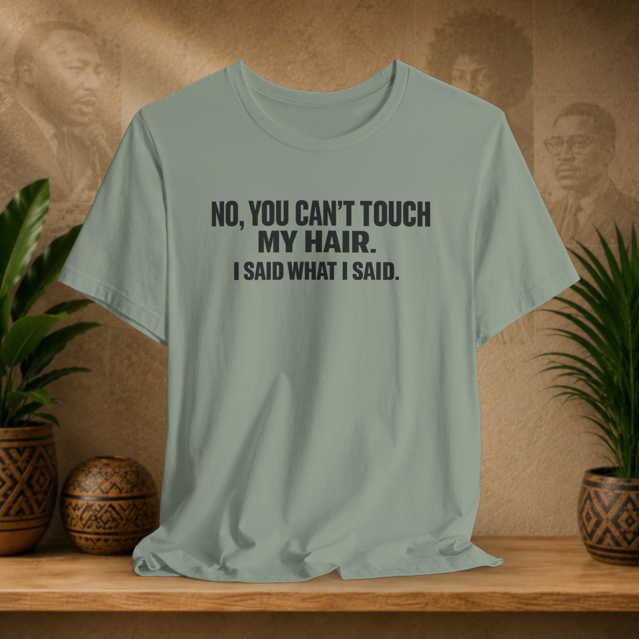 Light green t-shirt with text on a wooden surface with plants and a textured wall background