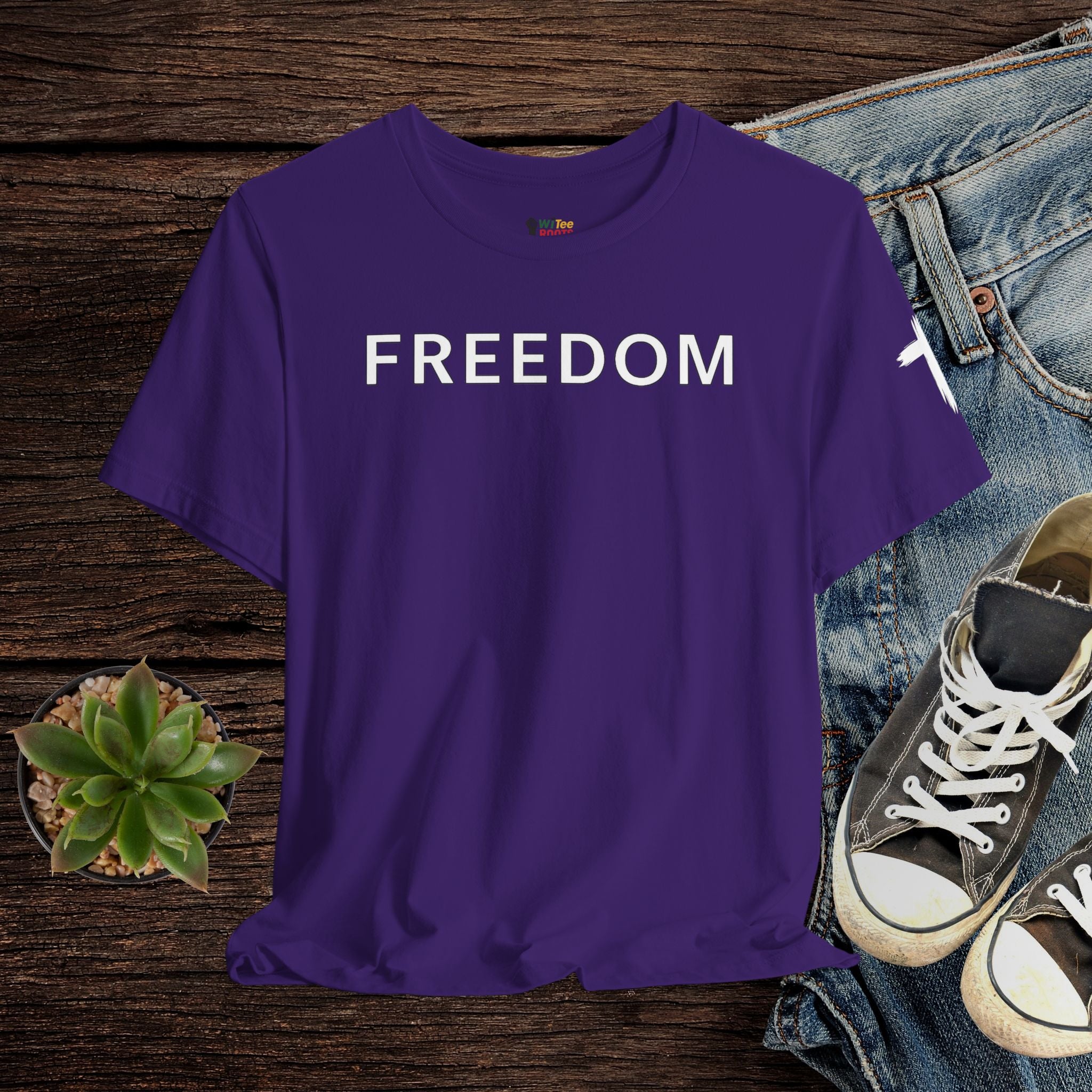 Purple t-shirt with 'FREEDOM' text on a wooden surface with jeans and sneakers.
