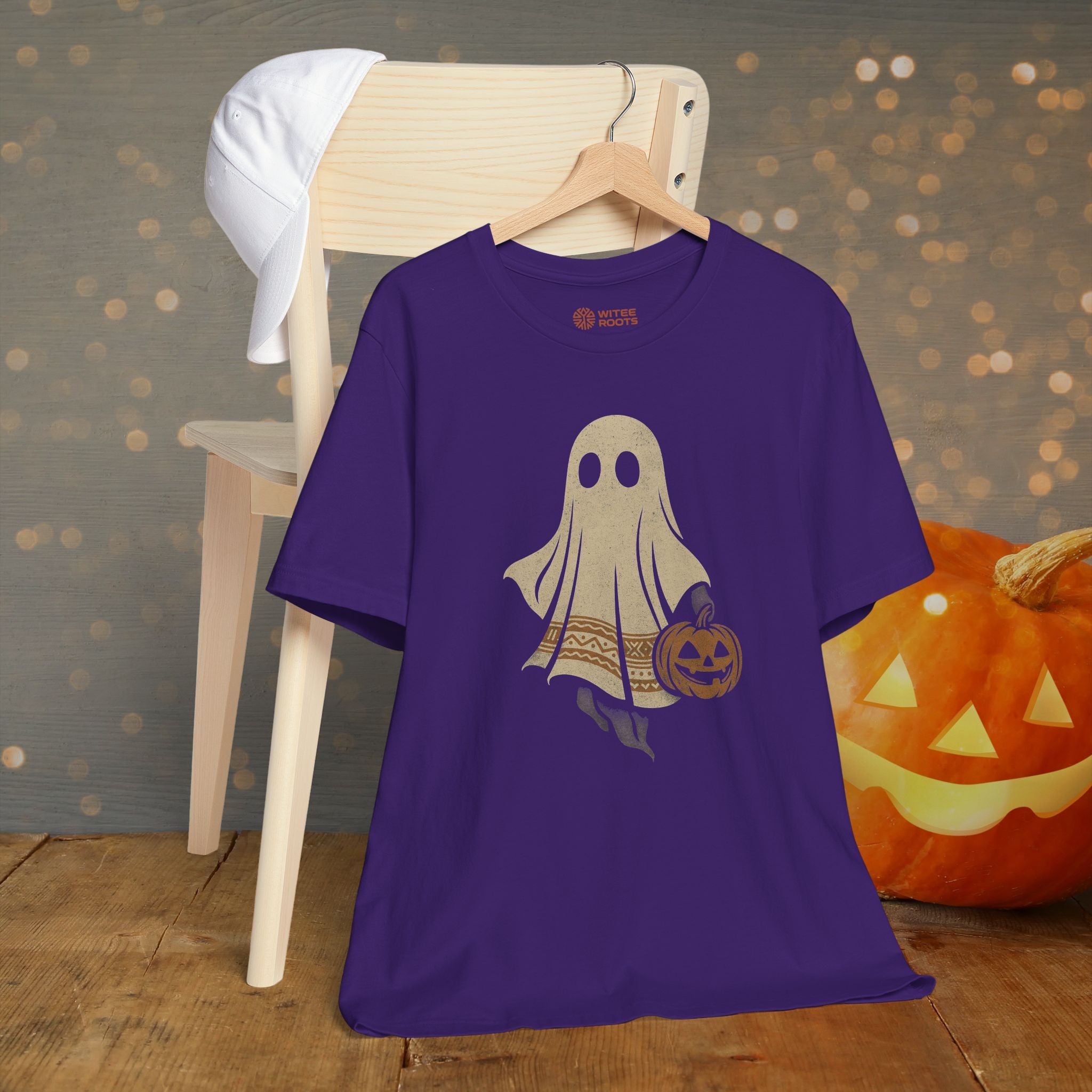 Purple t-shirt with ghost and pumpkin design on a wooden chair with a pumpkin in the background