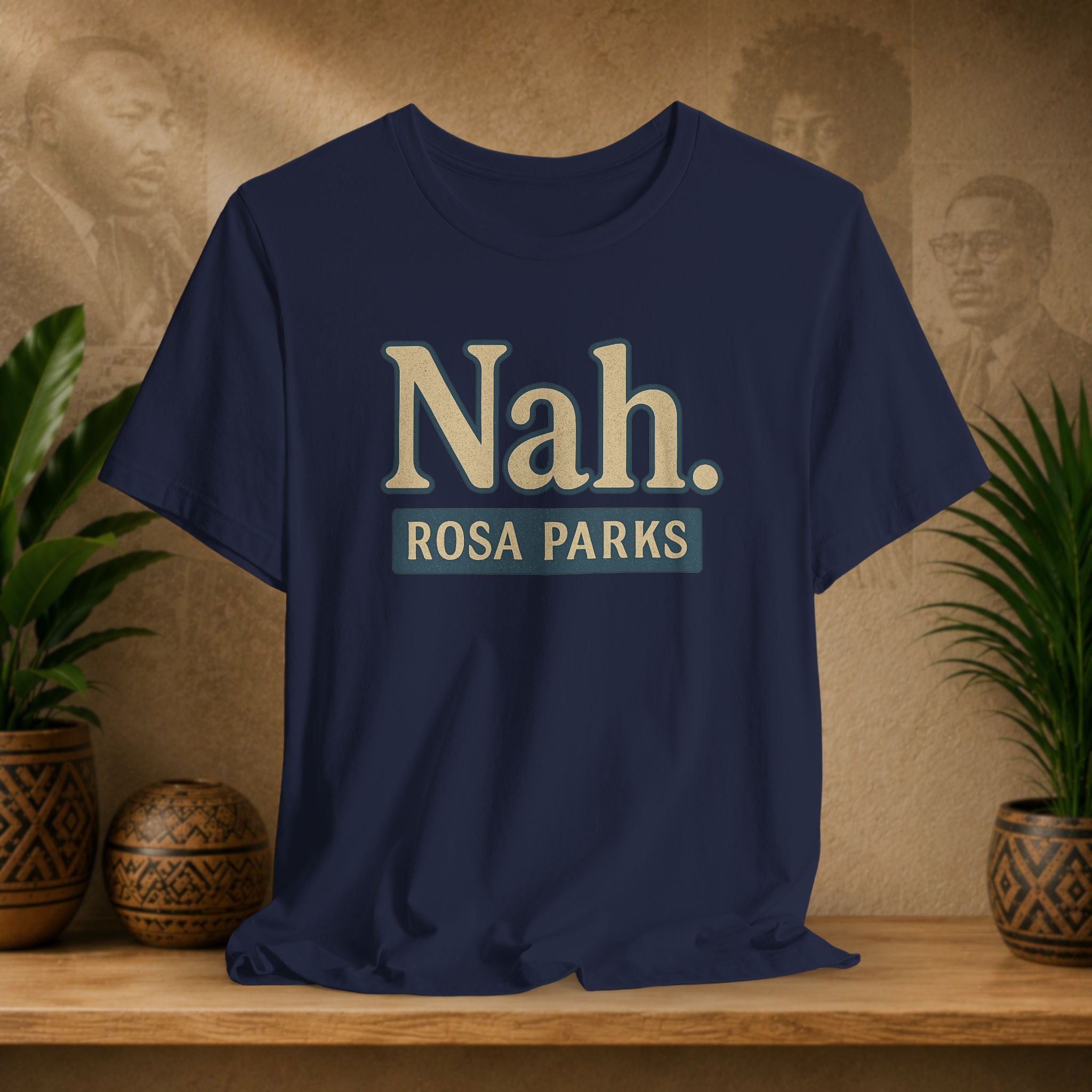 Navy blue t-shirt with 'Nah. ROSA PARKS' text on a wooden surface with plants and a vintage-style wall in the background.