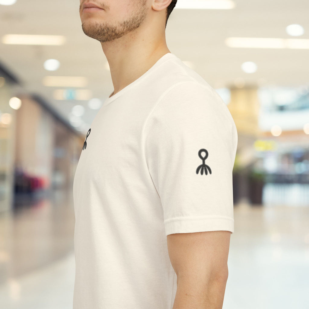 Person wearing a beige t-shirt with black logos in a blurred indoor setting