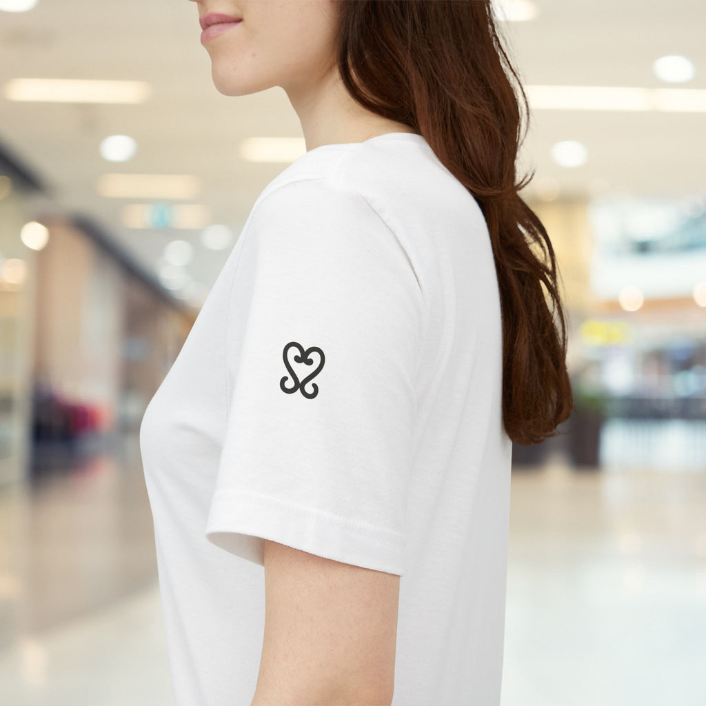 Person wearing a white t-shirt with a black heart design in a blurred indoor setting