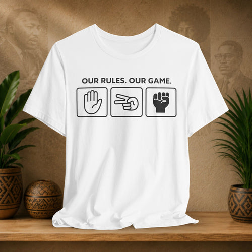 White t-shirt with graphic design and text on a wooden surface with plants and decorative items.