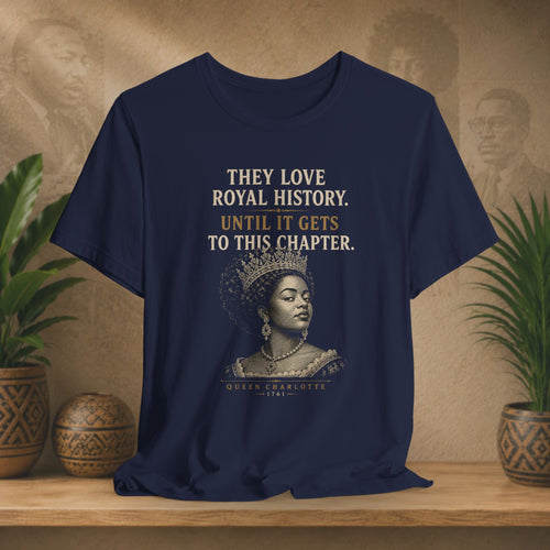 Navy blue t-shirt with a graphic of a woman in a crown and text on a wooden surface with plants.