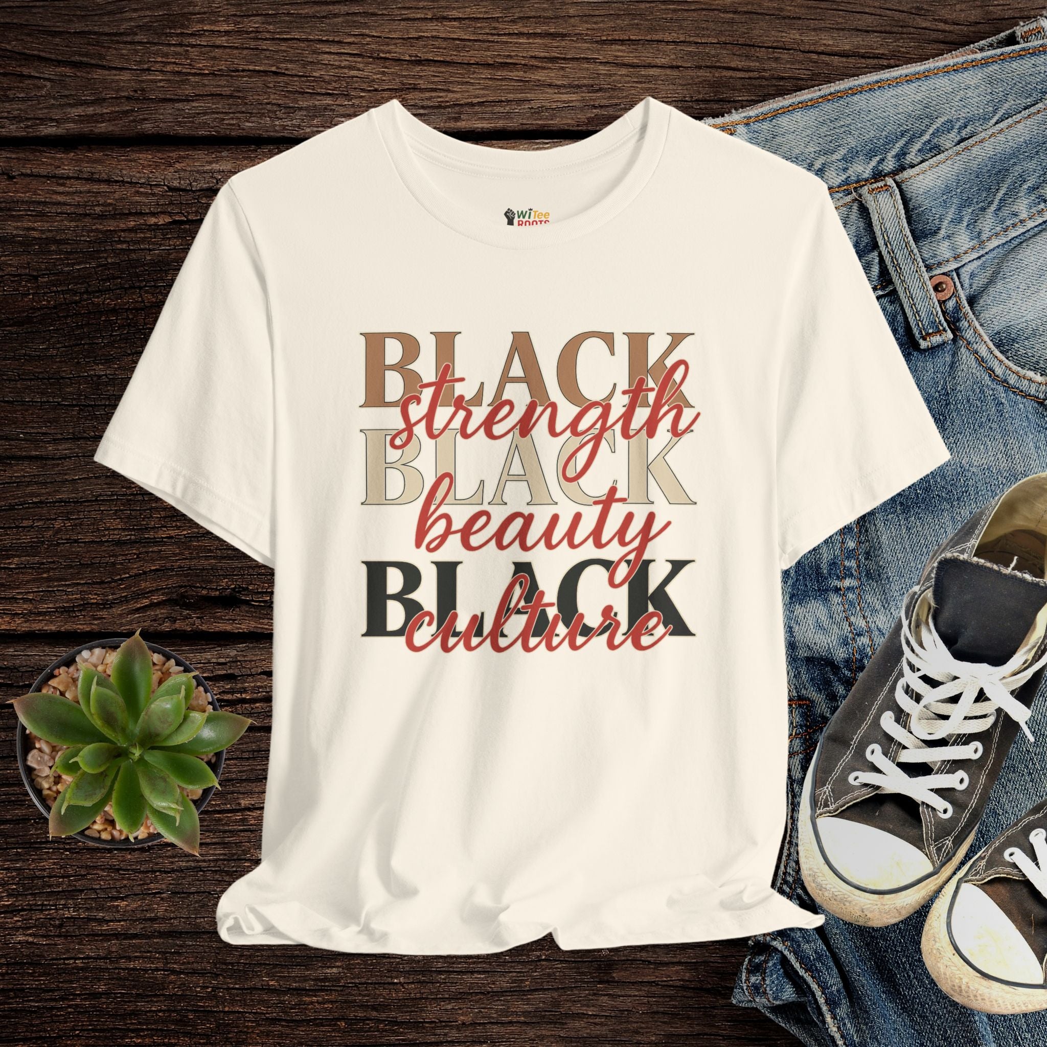 Beige t-shirt with 'BLACK strength BLACK beauty BLACK culture' text on a wooden surface with jeans and sneakers.