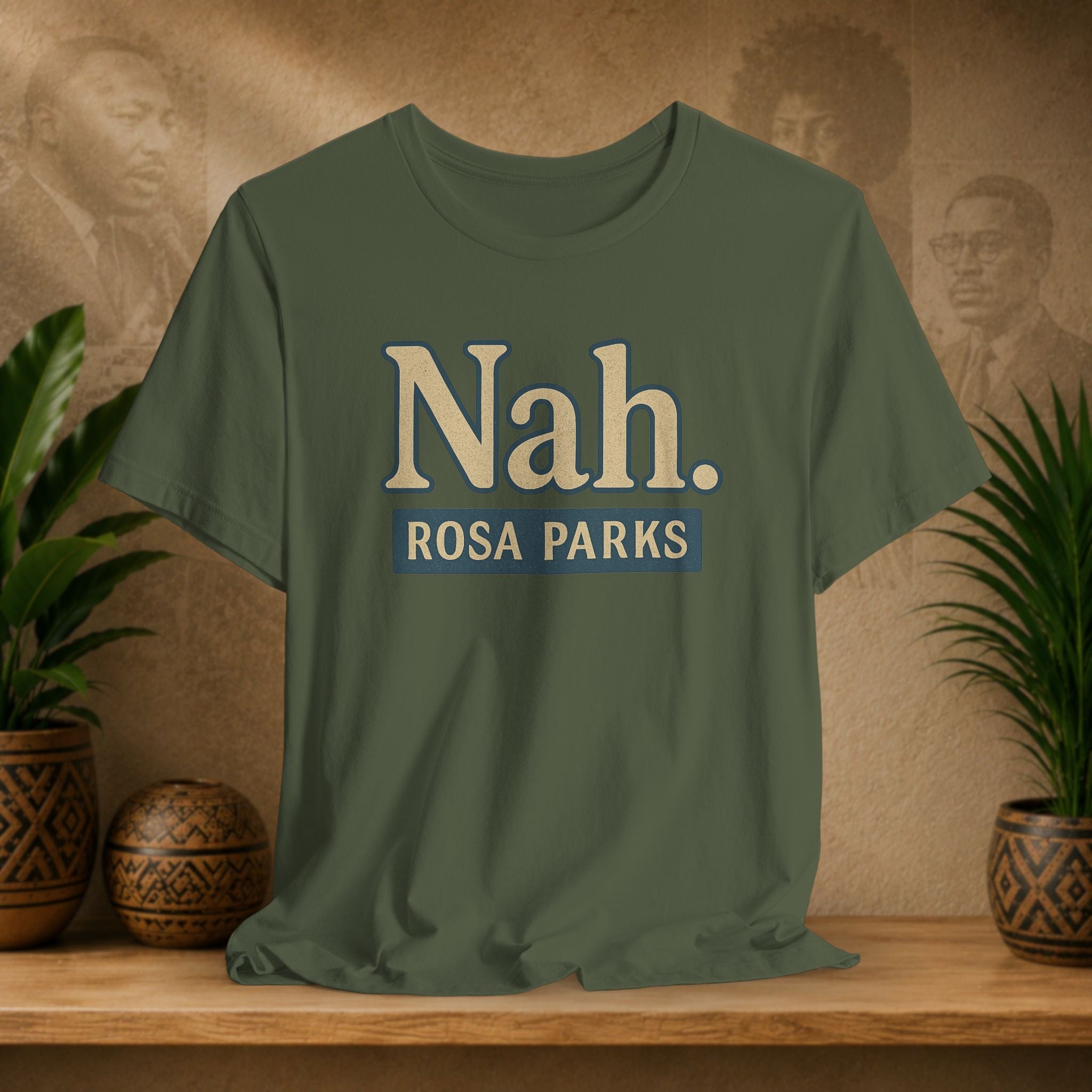 Green t-shirt with 'Nah. Rosa Parks' text on a wooden surface with decorative plants and background.
