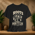 Black t-shirt with a family tree graphic and text on a wooden surface with plants and decorative items.