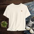 Beige t-shirt with a logo on a wooden surface with jeans and sneakers.