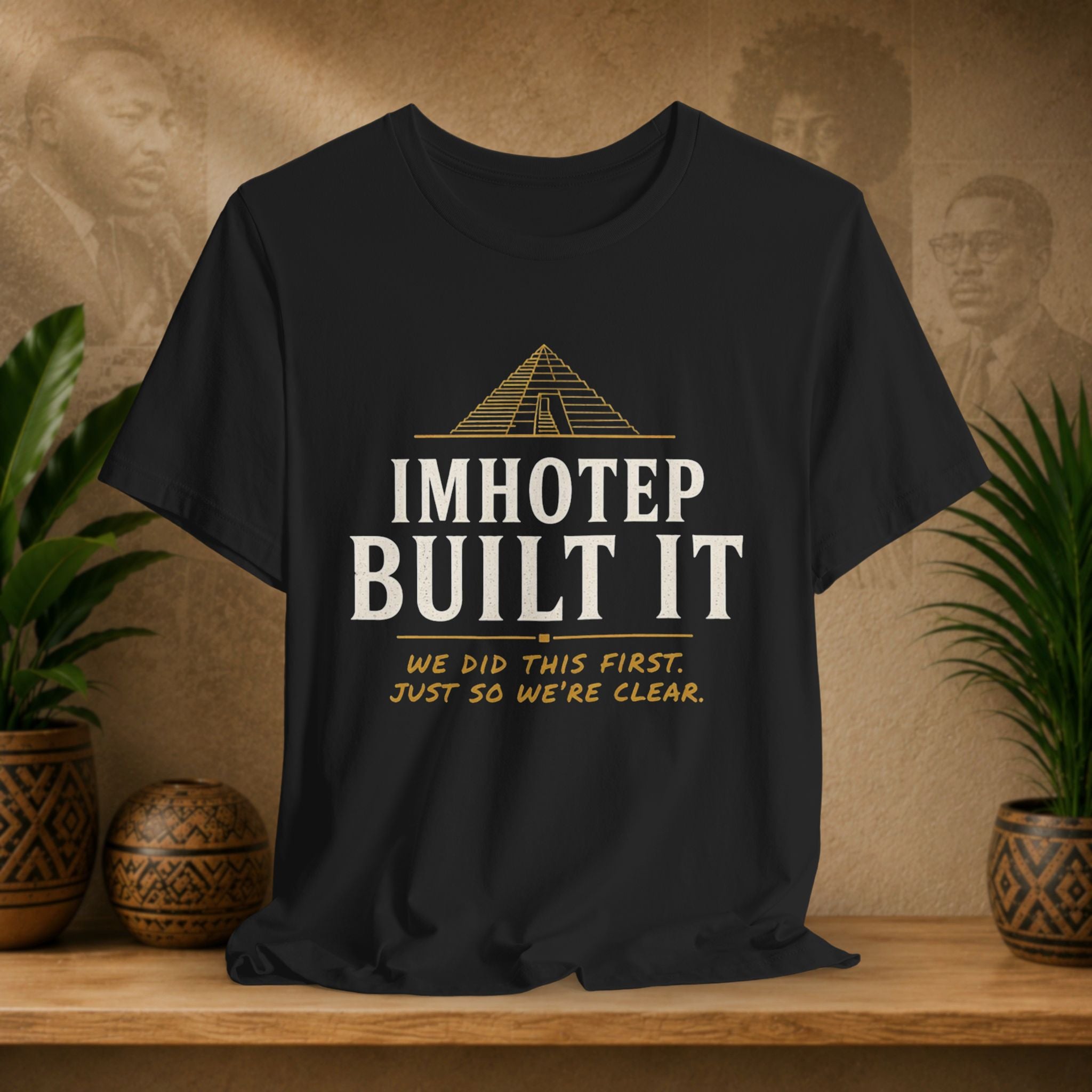 Black t-shirt with 'IMHOTEP BUILT IT' text on a wooden surface with decorative items.