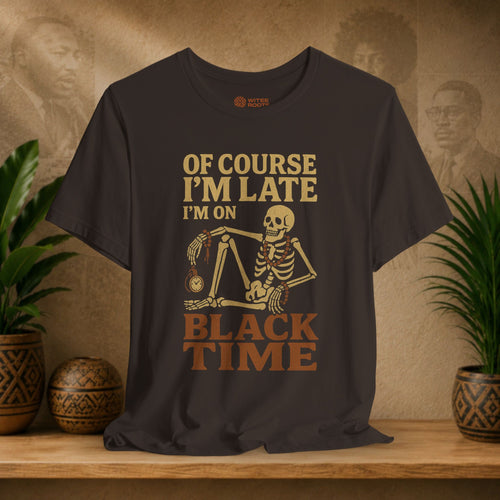 A brown graphic t-shirt displayed on a wooden shelf. The shirt features a vintage-style tan and brown graphic of a skeleton holding a clock, with the text 'OF COURSE I'M LATE I'M ON BLACK TIME'.