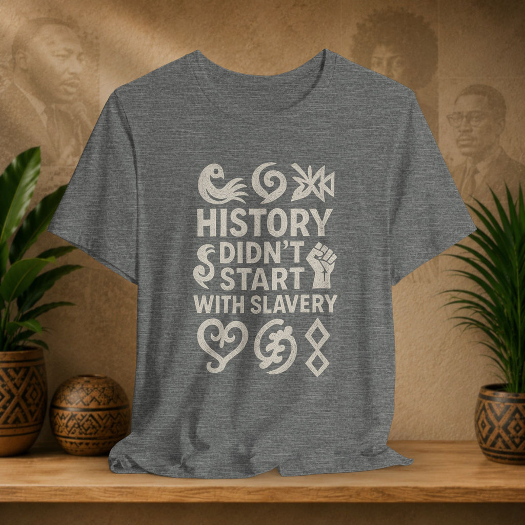Gray t-shirt with 'History didn't start with slavery' text on a wooden surface with decorative items.