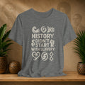 Gray t-shirt with 'History didn't start with slavery' text on a wooden surface with decorative items.