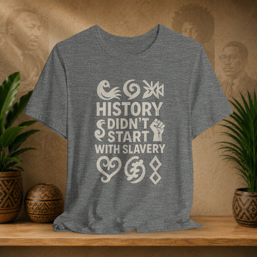 Gray t-shirt with 'History didn't start with slavery' text on a wooden surface with decorative items.
