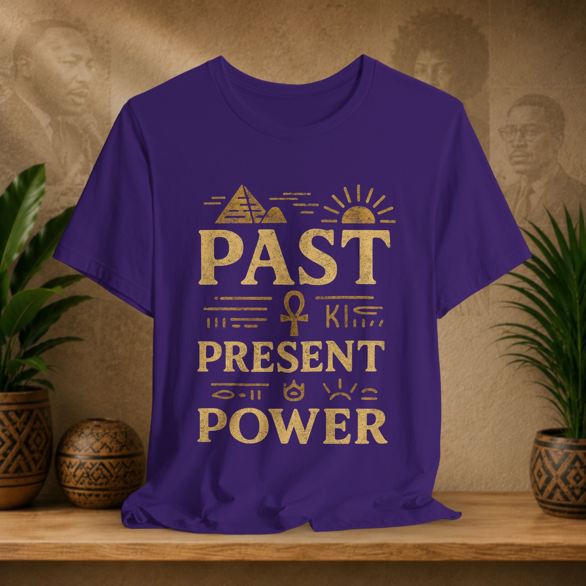 Purple t-shirt with gold text on a wooden surface with plants and decorative items in the background
