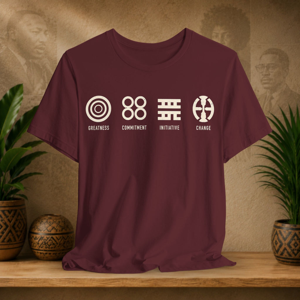 Maroon t-shirt with white symbols and text on a wooden surface with plants and wall art in the background