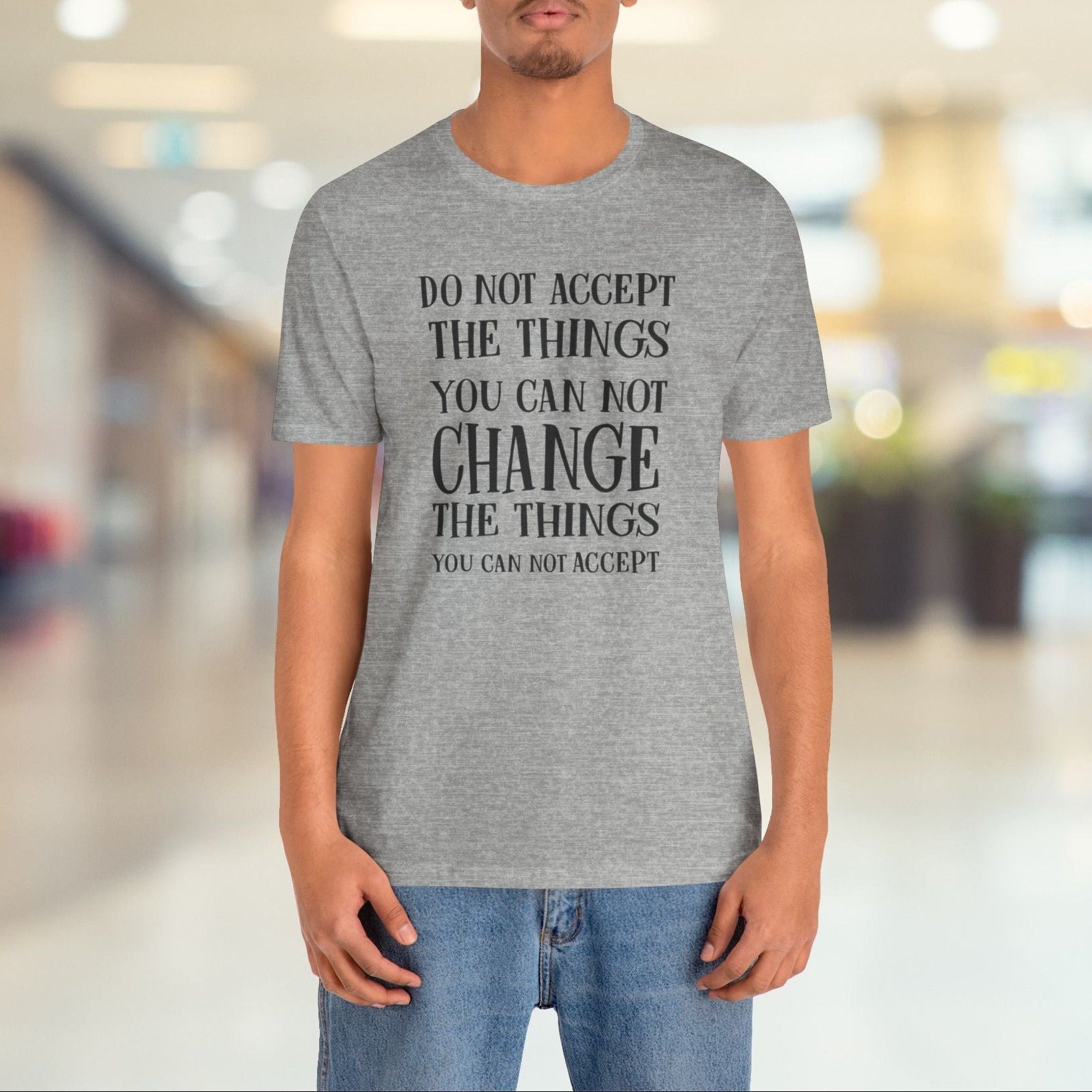 Person wearing a gray t-shirt with a motivational quote in a blurred indoor setting