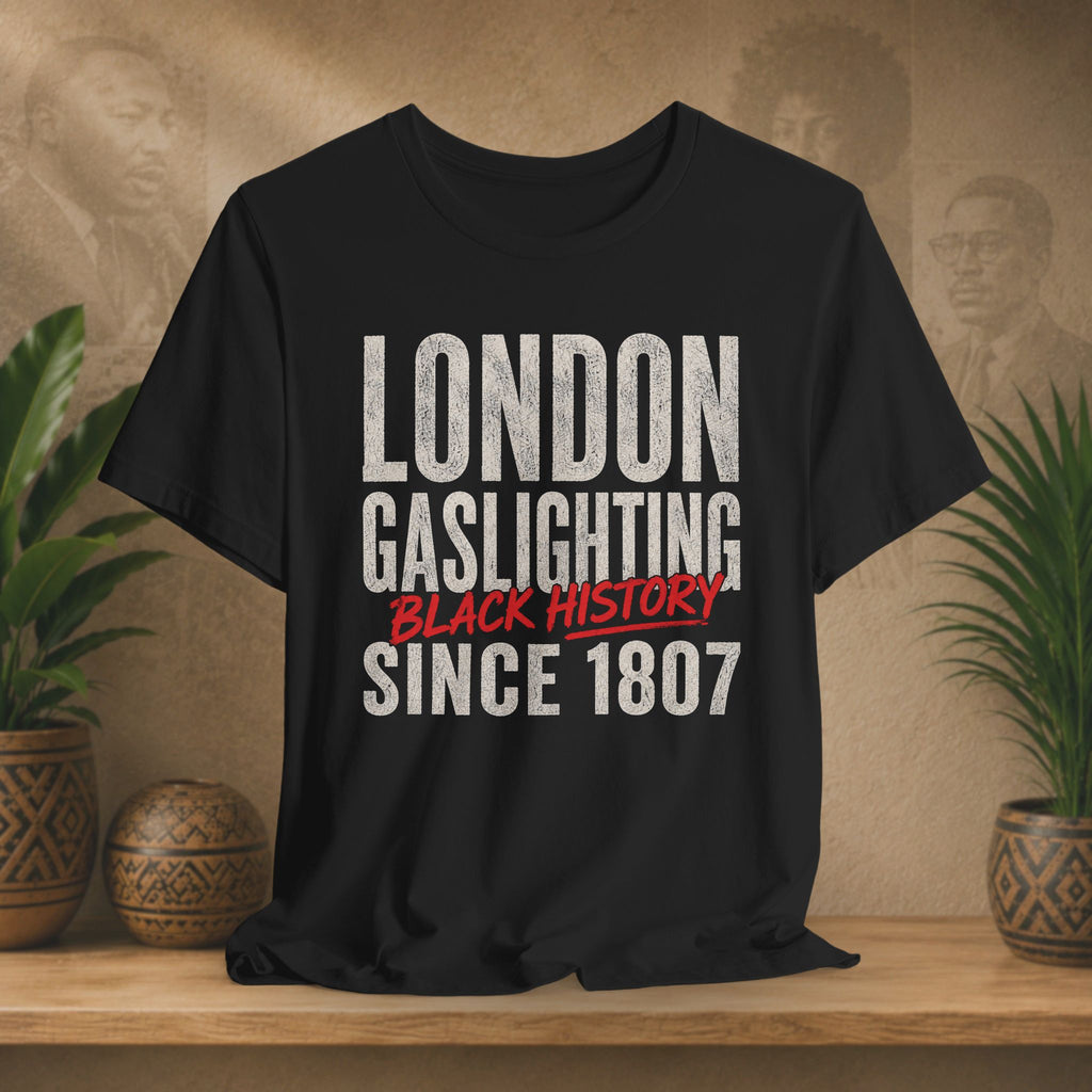 Black t-shirt with 'London Gaslighting Black History Since 1807' text on a wooden surface with plants and a textured wall background.