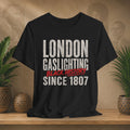 Black t-shirt with 'London Gaslighting Black History Since 1807' text on a wooden surface with plants and a textured wall background.