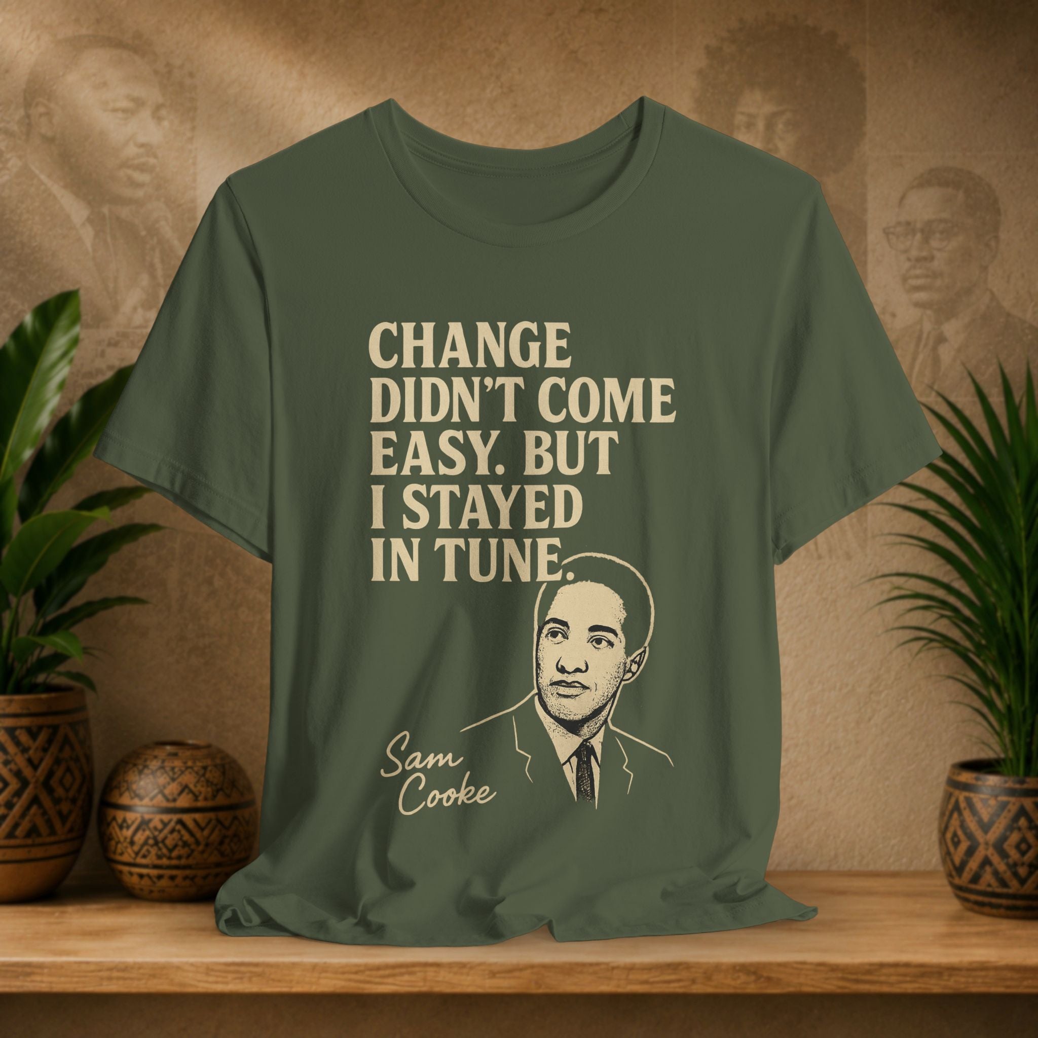 Green t-shirt with text and portrait of Sam Cooke on a wooden surface with plants and wall art in the background.