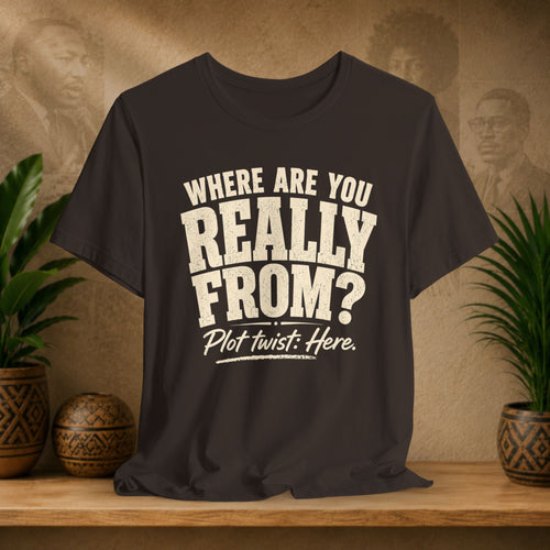 Brown t-shirt with white text on a wooden surface with plants and a textured wall background