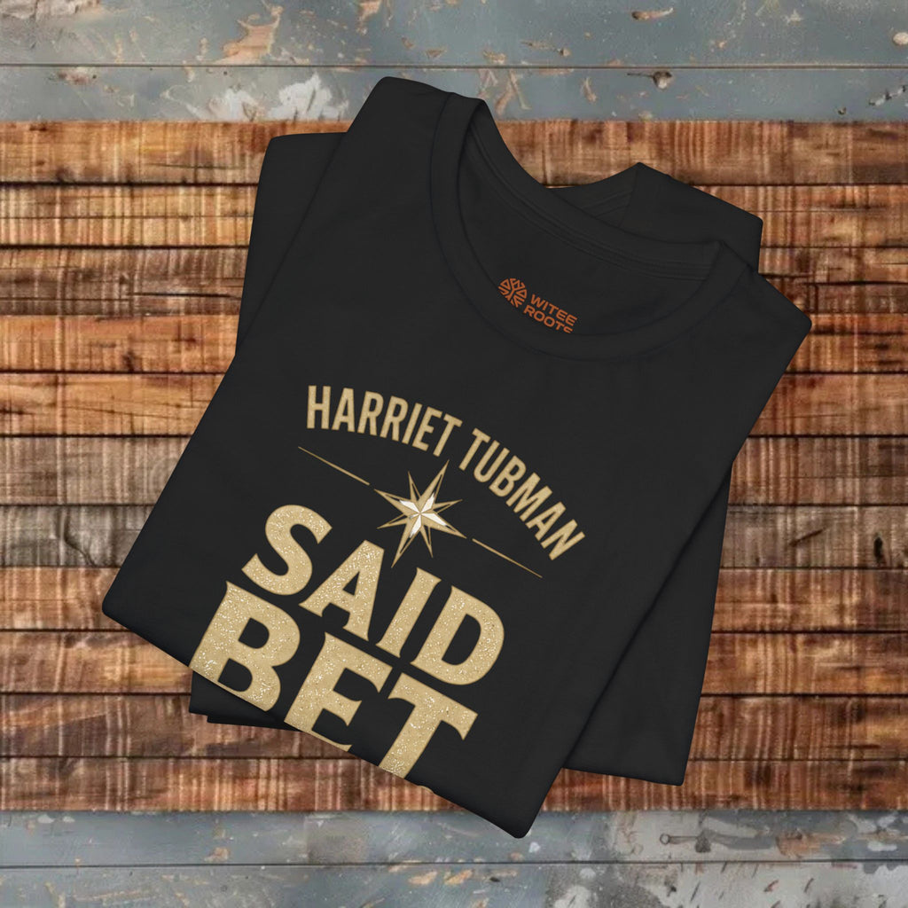 Folded black t-shirt with 'Harriet Tubman Said Bet' text on a wooden surface