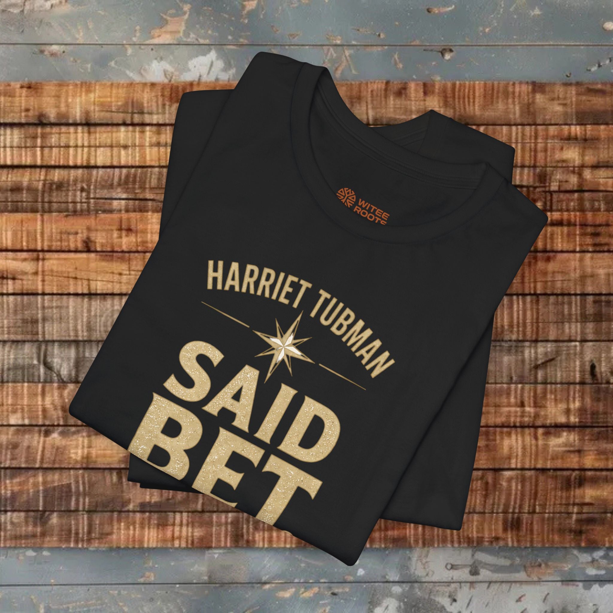 Folded black t-shirt with 'Harriet Tubman Said Bet' text on a wooden surface