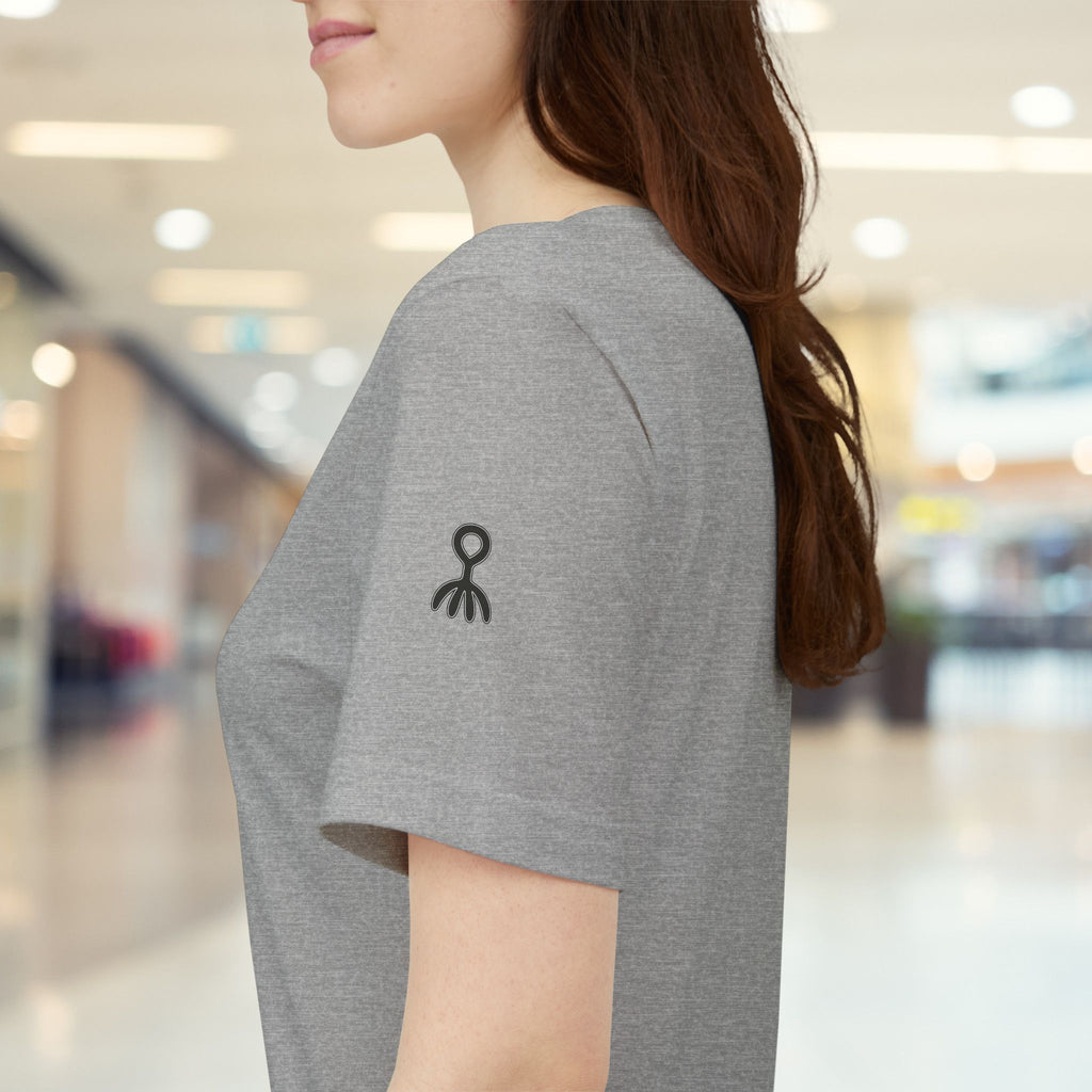 Person wearing a grey t-shirt with black logos in a blurred indoor setting