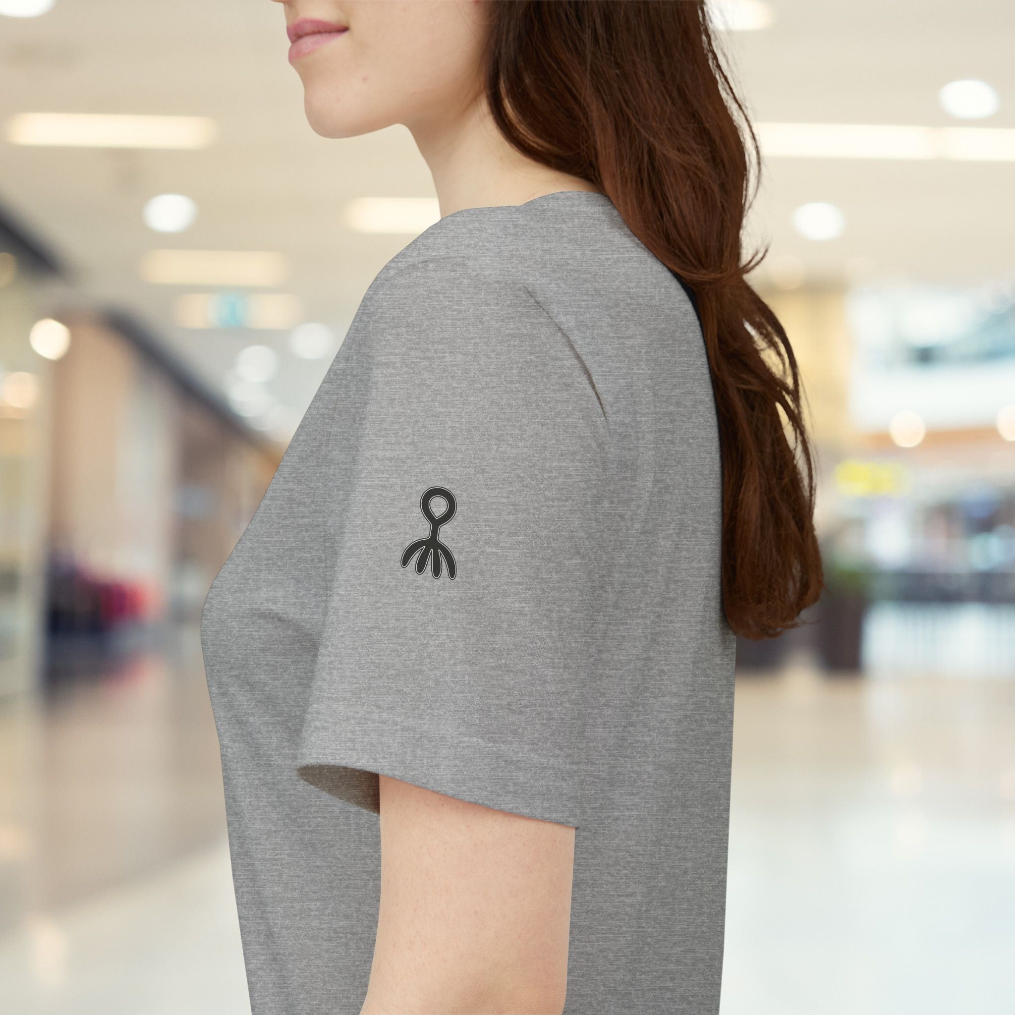 Person wearing a grey t-shirt with black logos in a blurred indoor setting