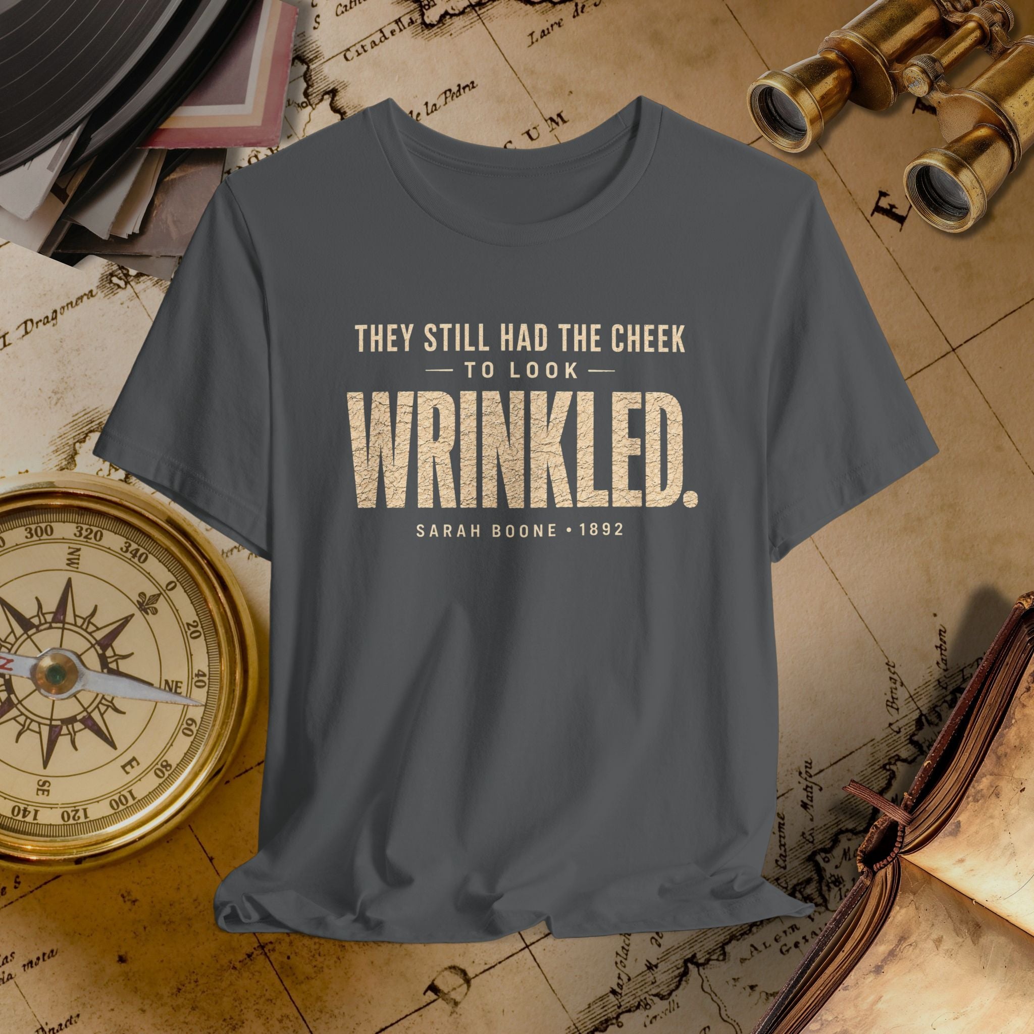 Gray t-shirt with humorous quote on a vintage background with books and binoculars.