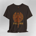 Black t-shirt with a graphic design of a woman in a meditative pose and 'STILL RISE' text on a gray background