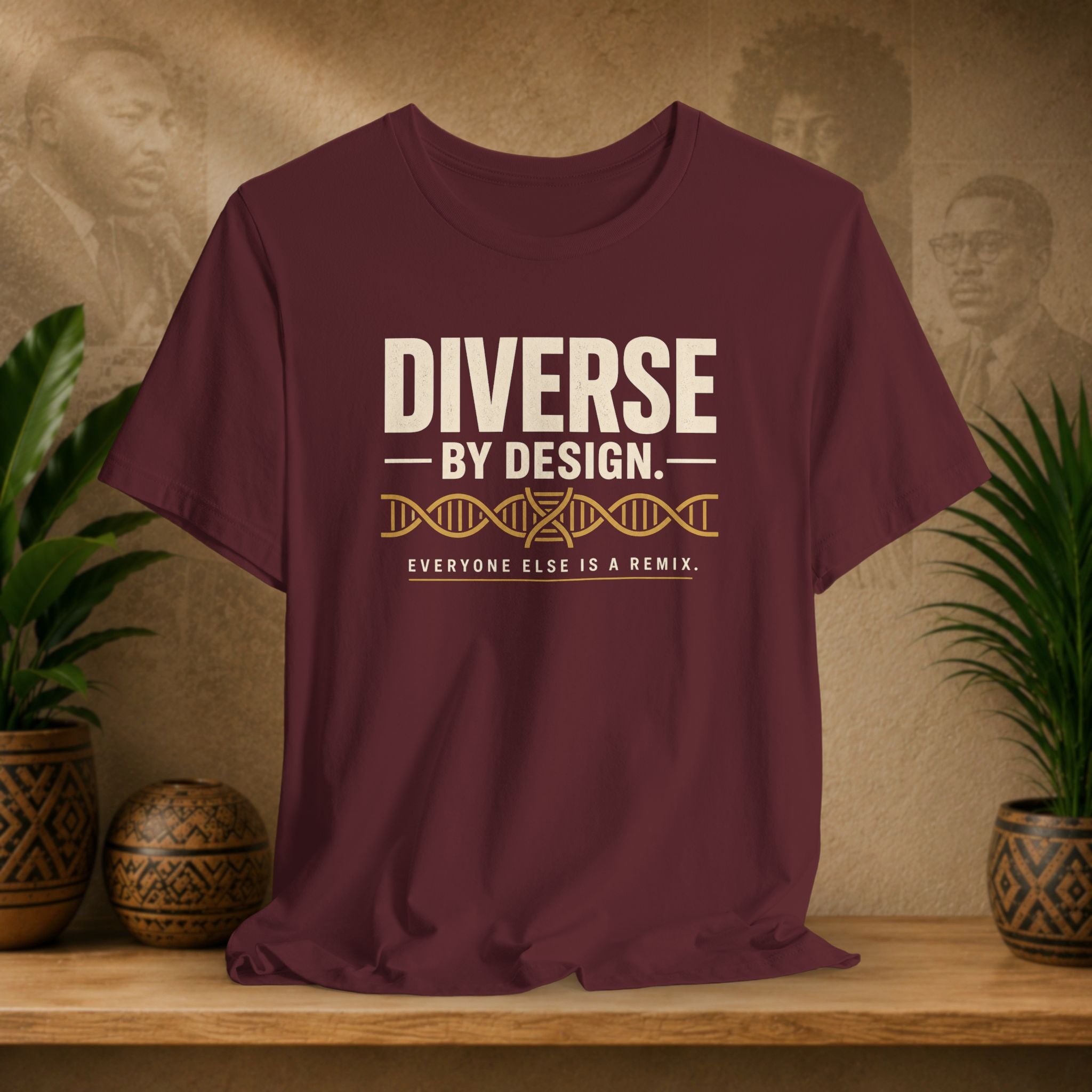 Maroon t-shirt with 'Diverse by Design' text on a wooden surface with decorative plants and background.