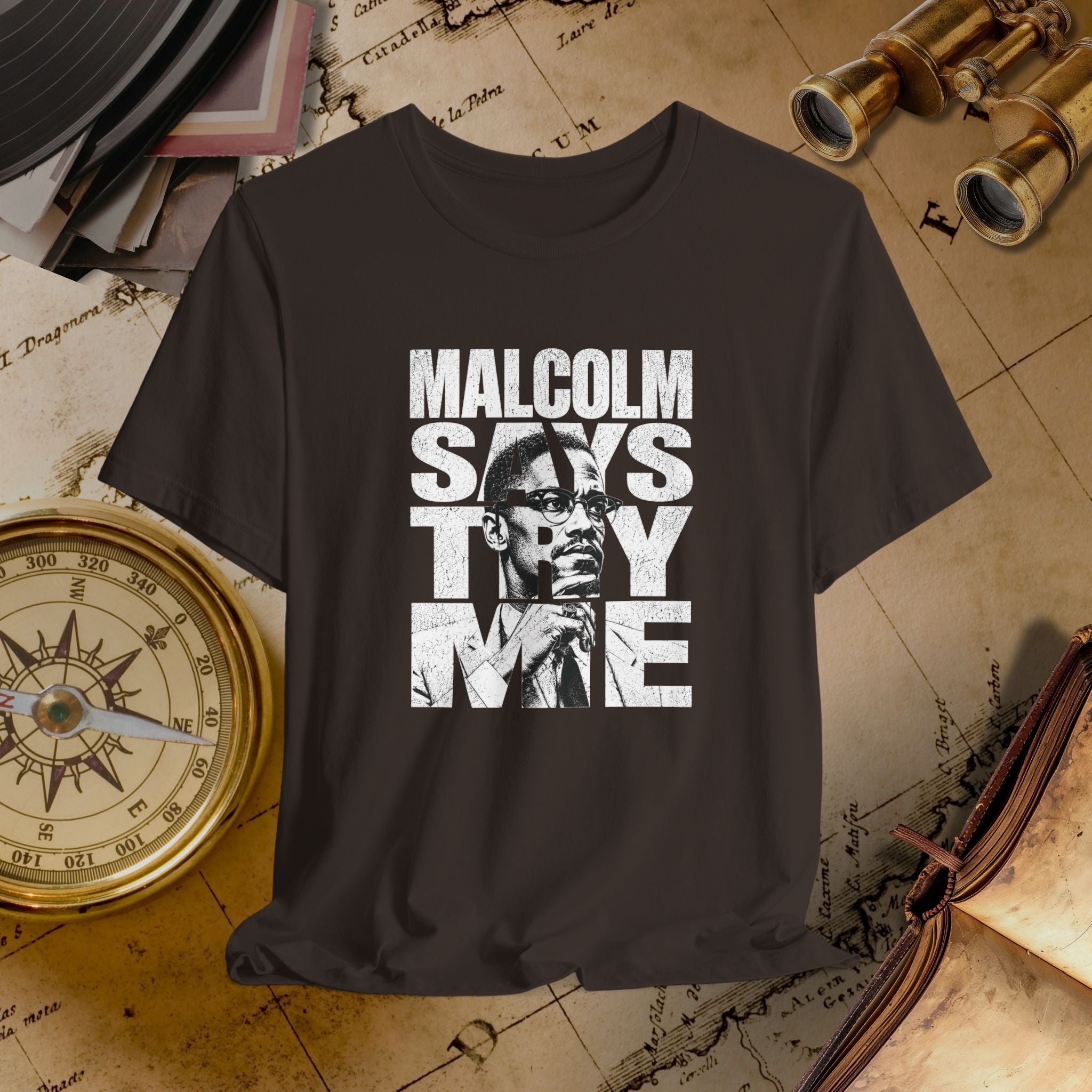 Brown t-shirt with 'Malcolm Says Thy Name' graphic on a vintage map background