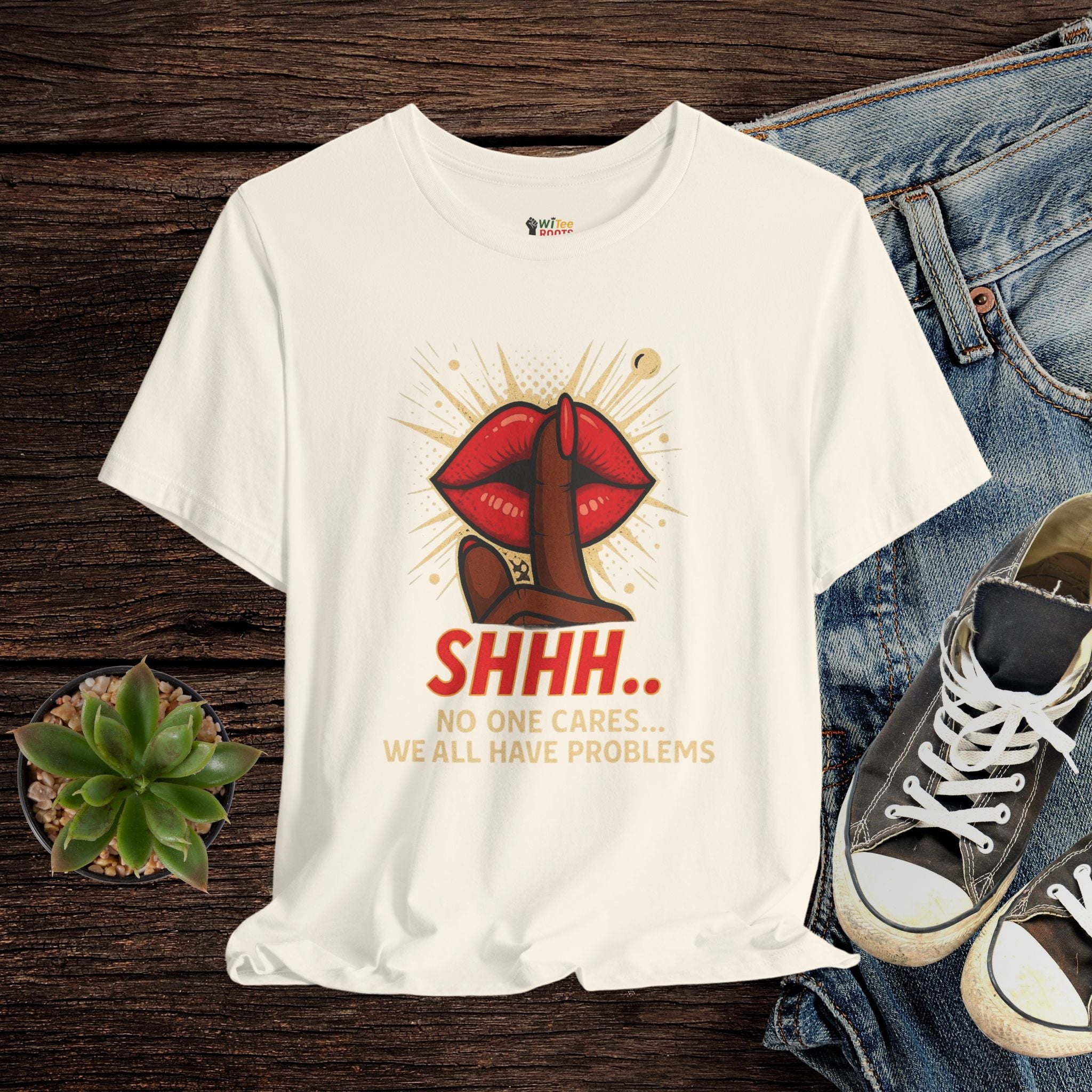 Beige t-shirt with graphic design and text on a wooden surface with jeans and sneakers.