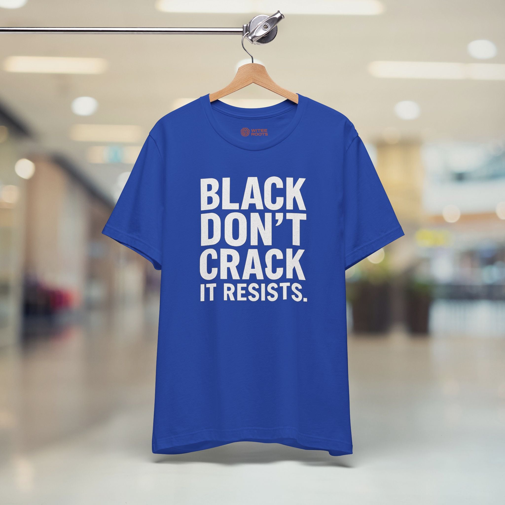 Blue t-shirt with white text 'BLACK DON'T CRACK IT RESISTS.' on a hanger in a blurred indoor setting.