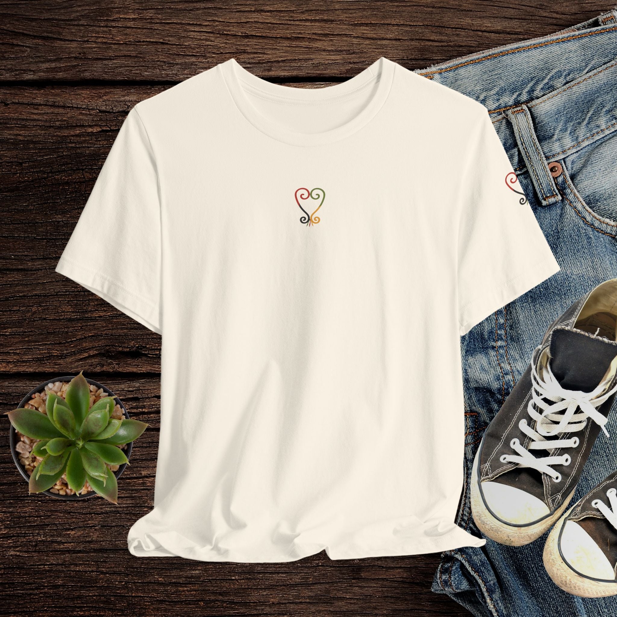 Beige t-shirt with a small design on a wooden surface with jeans and sneakers.