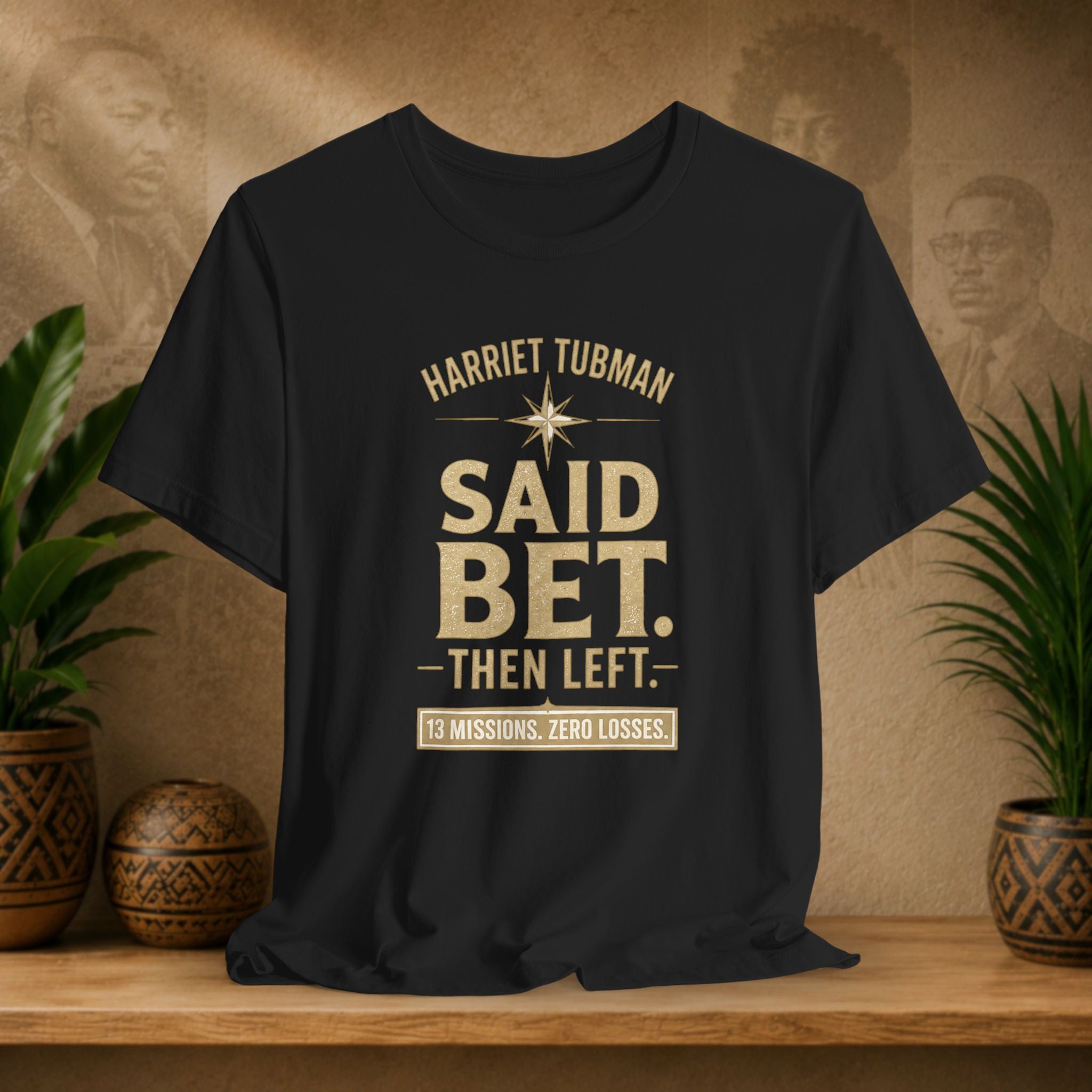 Black t-shirt with text on a wooden surface with plants and decorative items.