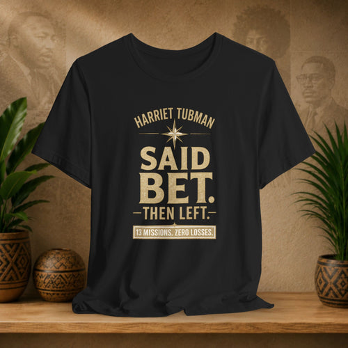 Black t-shirt with text on a wooden surface with plants and decorative items.