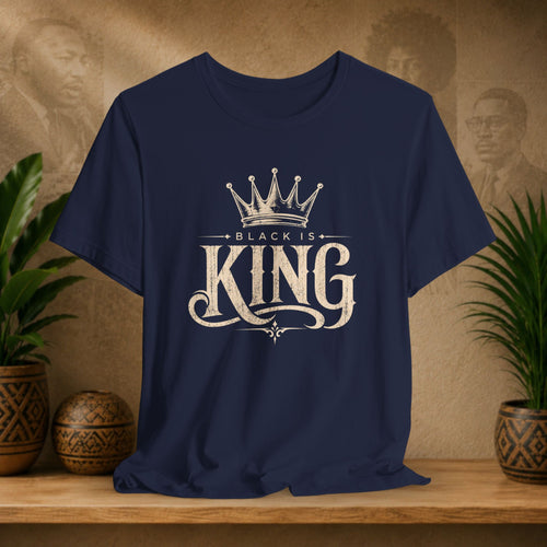 Navy blue t-shirt with 'Black is King' design on a wooden surface with plants and decorative items.
