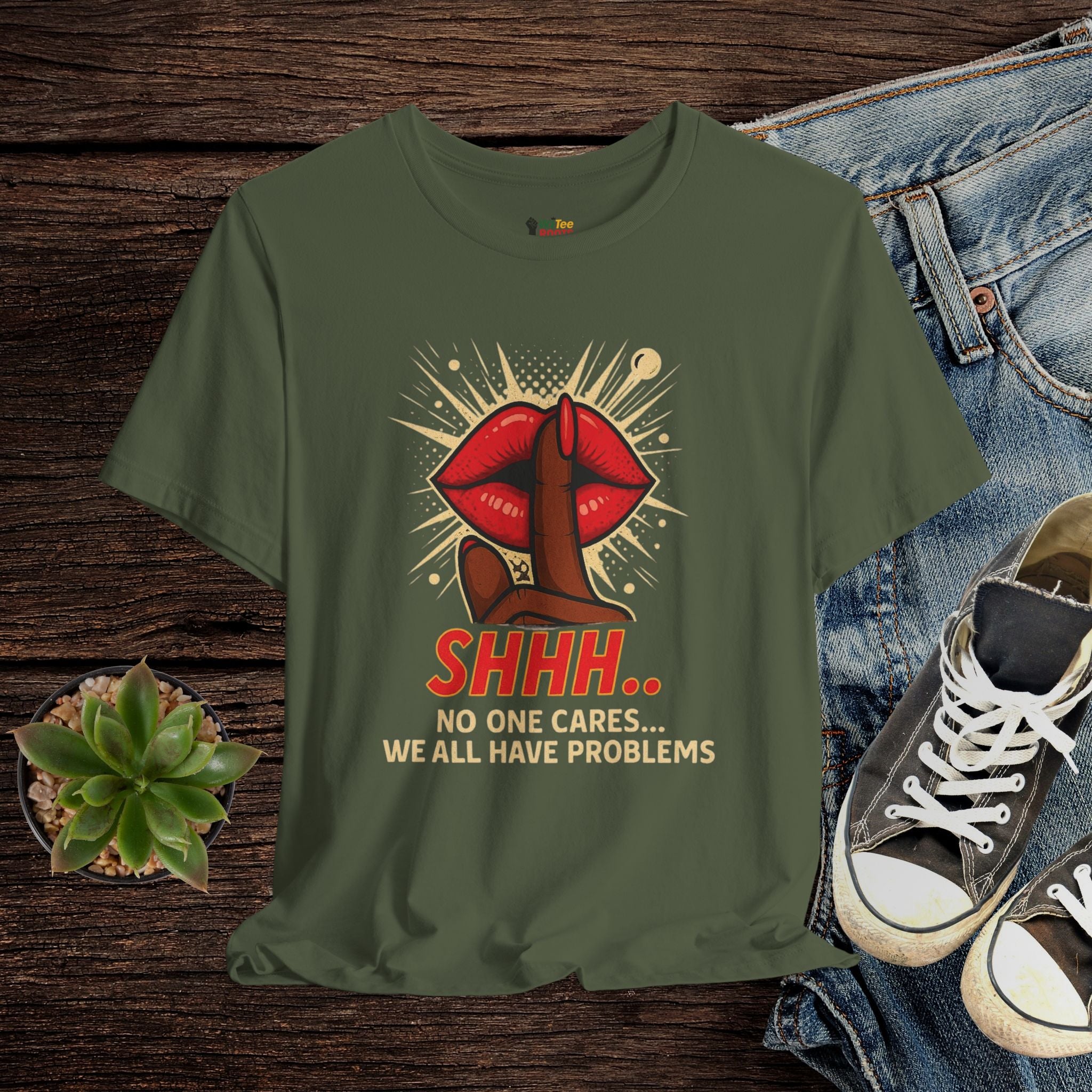 Green t-shirt with graphic design and text on a wooden surface with jeans and sneakers.