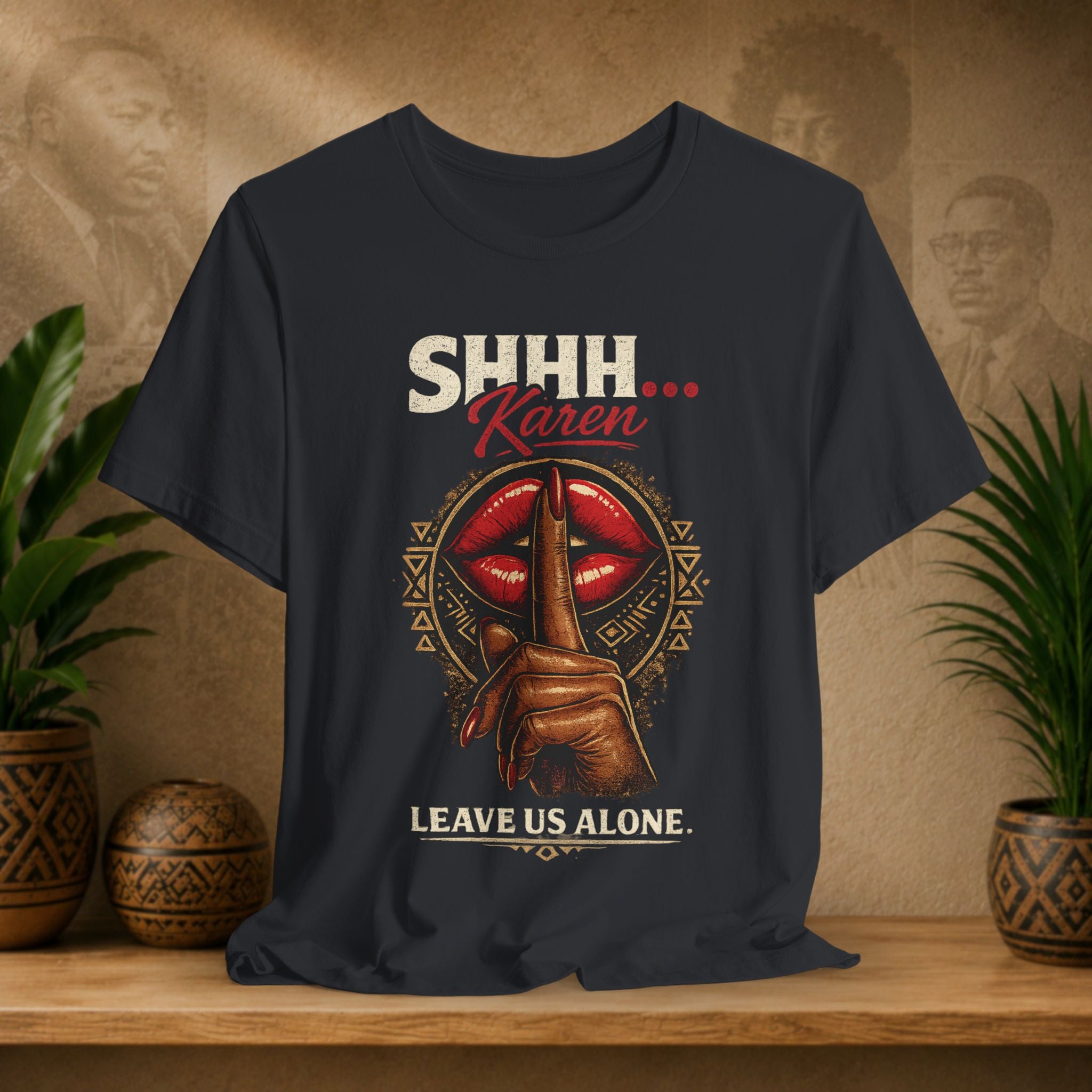A black graphic t-shirt displayed on a wooden shelf. The shirt features a graphic design with the text 'SHHH’.