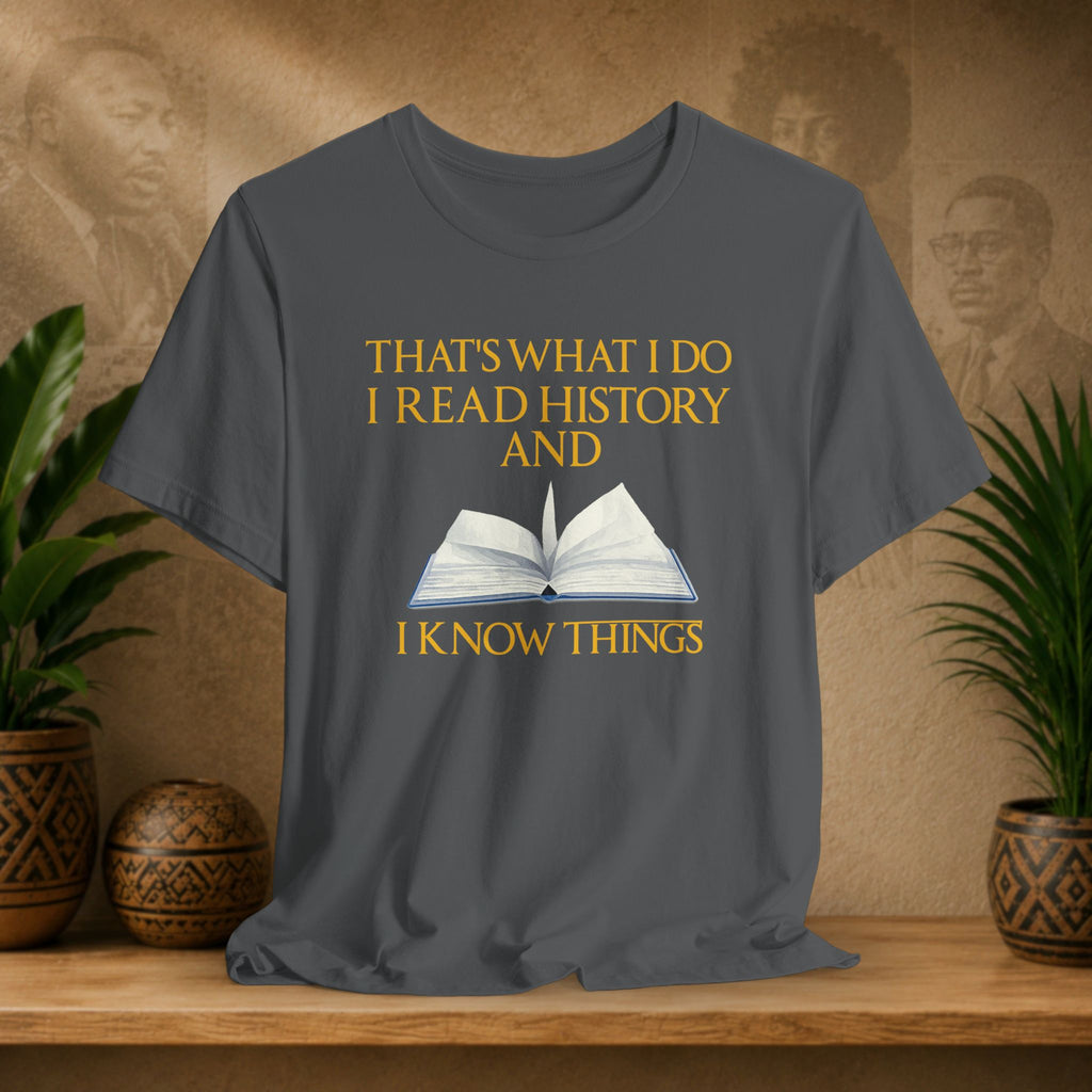 Gray t-shirt with a book graphic and text on a wooden surface with plants and a textured wall background