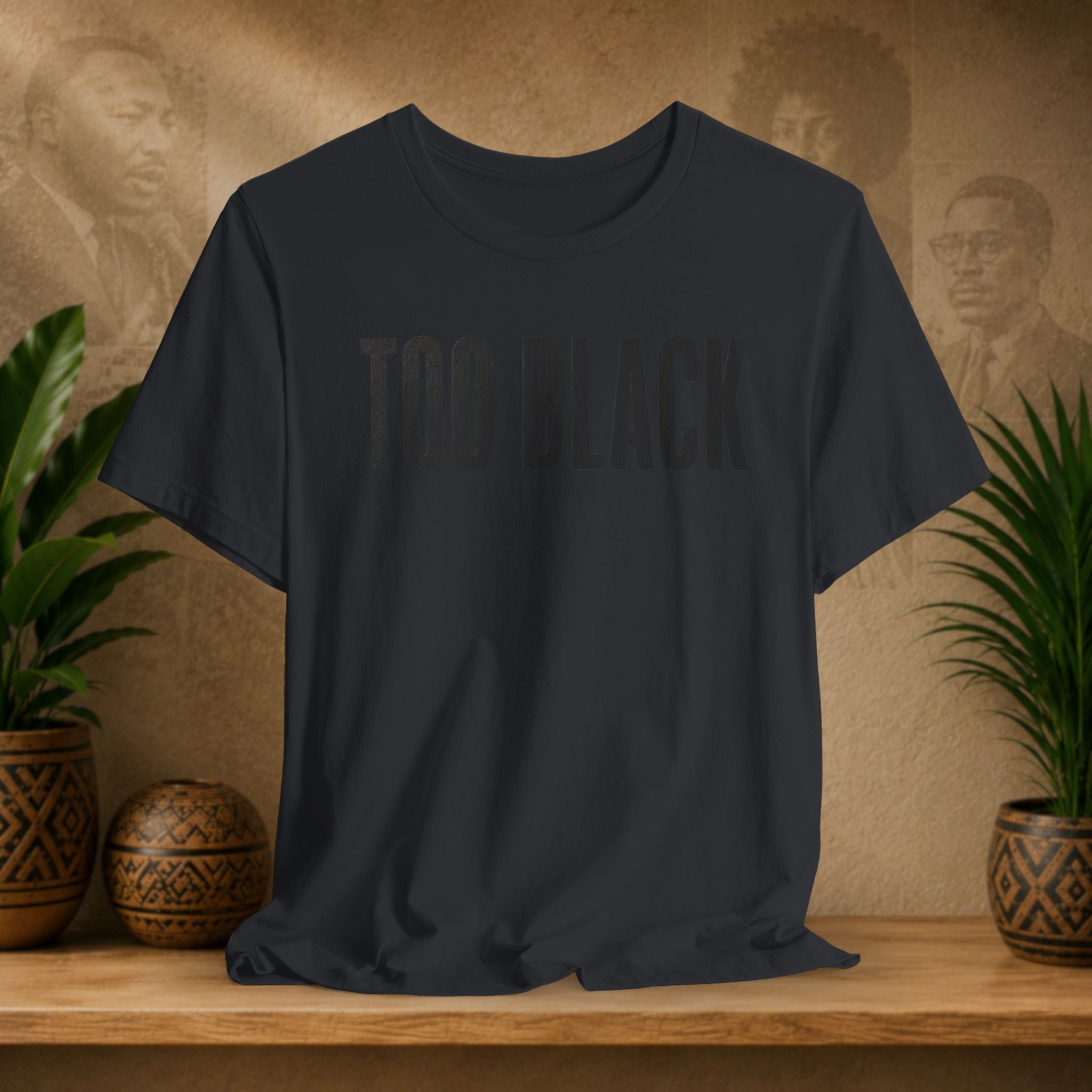 Vintage Black t-shirt with 'TOO BLACK' text on a wooden shelf with plants and decorative items.