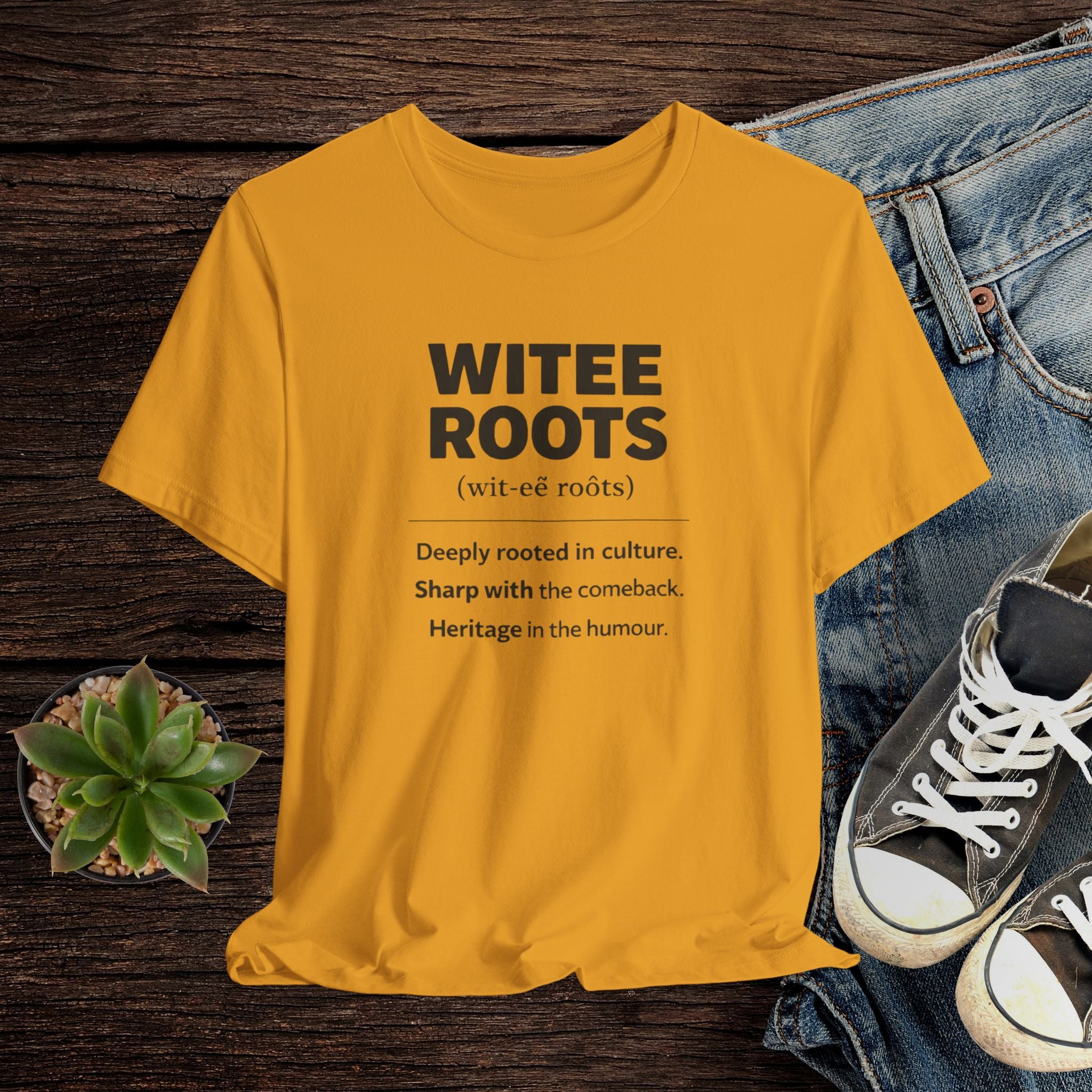Yellow t-shirt with 'WITEE ROOTS' text on a wooden surface with jeans and sneakers.