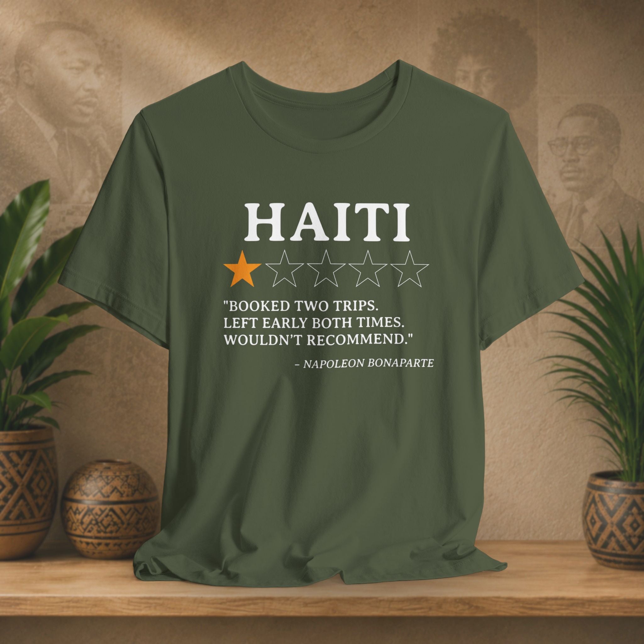 Green t-shirt with Haiti-themed text and rating on a wooden surface with plants and a textured wall background.
