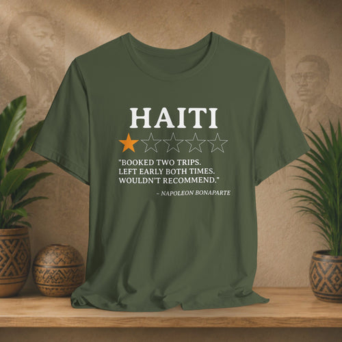 Green t-shirt with Haiti-themed text and rating on a wooden surface with plants and a textured wall background.