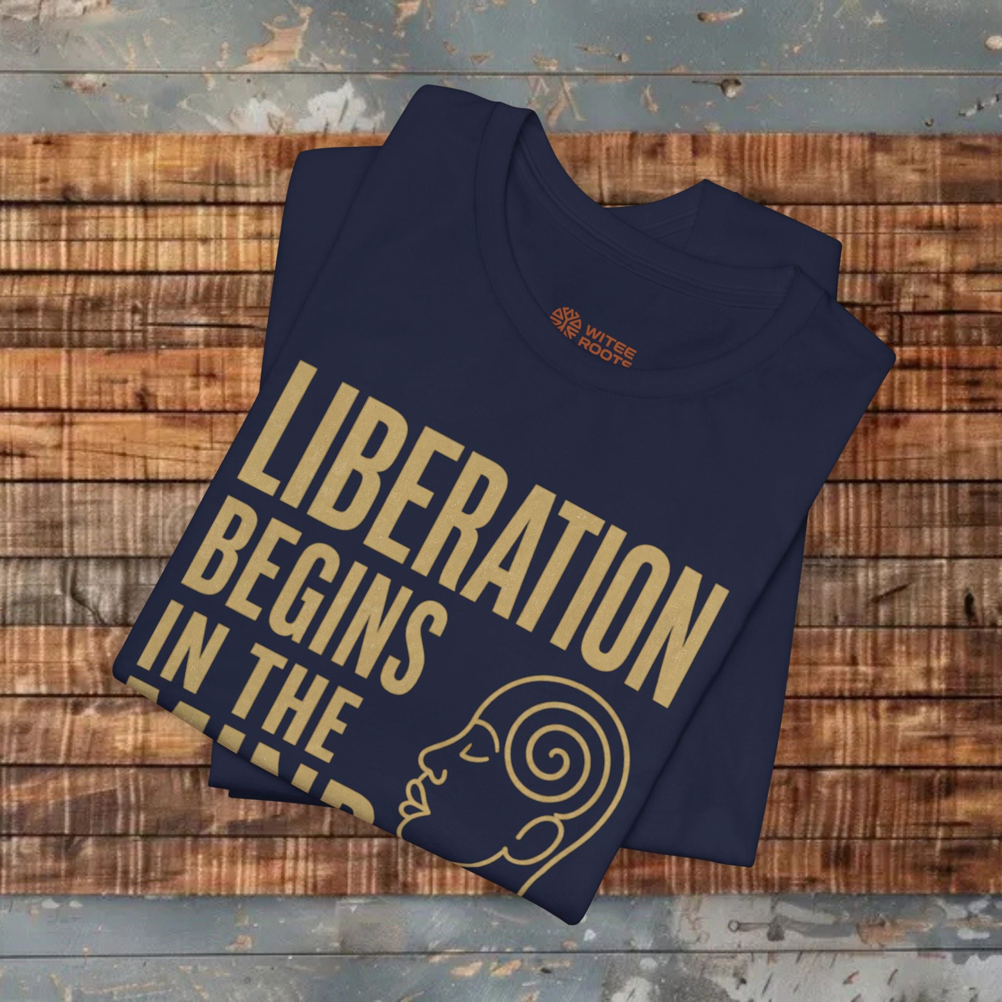 Folded navy blue t-shirt with 'Liberation Begins in the' text on a wooden surface