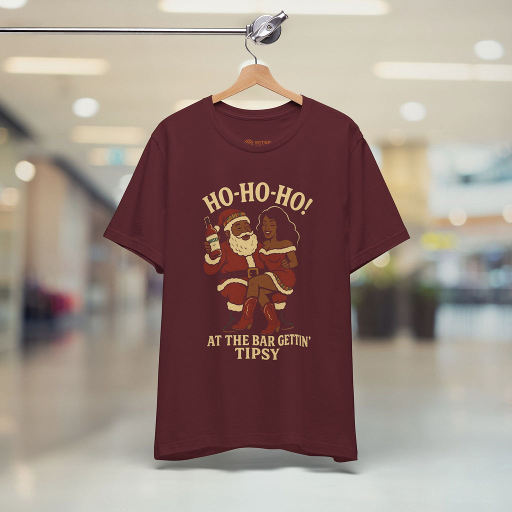 Maroon t-shirt with Christmas-themed design on a hanger in a store.